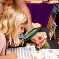 young girl examining vial through a magnifying glass at student exhibit table